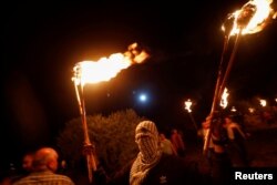 Demonstran Palestina memegang obor saat protes malam menentang permukiman Israel di Beita di Tepi Barat yang diduduki Israel, 22 Juni 2021. (Foto: Reuters)