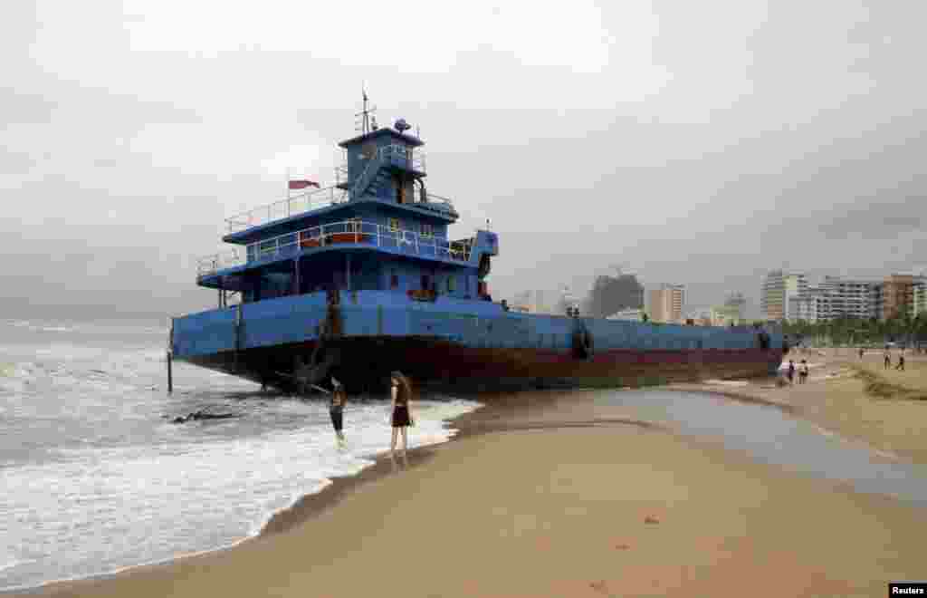 People stand on a beach next to a stranded boat which was pushed ashore by waves under the influence of typhoon Kujira, in Sanya, Hainan province, China, June 23, 2015.