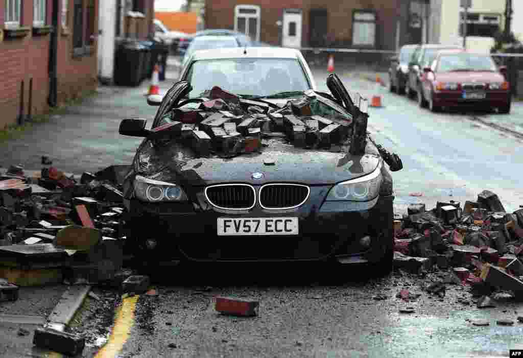 A parked car is crushed by masonry after high winds forced the gable end of an apartment block to collapse in Leigh, north west England.