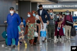 Keluarga Afghanistan yang dievakuasi dari Kabul, berjalan melalui terminal untuk naik bus setelah mereka tiba di Bandara Internasional Washington Dulles, 31 Agustus 2021. (Foto: AP)