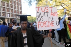 A jobless university graduate poses for a photo while holding a banner with a message directed at Zimbabwean President Robert Mugabe during protests in Harare on Aug. 3, 2016.