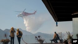 Firefighters watch as a helicopter drops water in a wildfire in the Pacific Palisades area of Los Angeles, Monday, Oct. 21, 2019. 