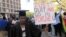 FILE: A jobless university graduate poses for a photo while holding a banner with a message directed at Zimbabwean President Robert Mugabe during protests in Harare on Aug. 3, 2016.