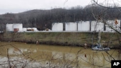 Para pekerja memeriksa daerah di luar dinding sekitar tangki penyimpanan yang membocorkan bahan kimia ke Sungai Elk di fasilitas penyimpanan Freedom Industries di Charleston, West Virginia. 