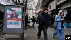 Orang-orang berjalan melewati poster pemilu Hamid Abdolmaleki, kandidat parlemen untuk pemilu 1 Maret mendatang, di pusat ibu kota Teheran, Kamis (22/2). 