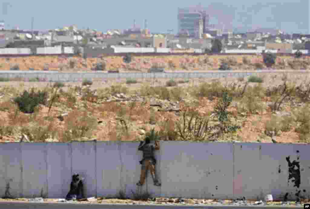 Rebel fighters observe the fighting near the main Moammar Gadhafi compound in Bab Al-Aziziya district in Tripoli, LIbya, Tuesday, Aug. 23, 2011, where some of the heaviest fighting took place. The compound, which has been heavily damaged by NATO airstrike