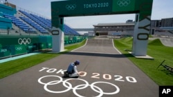 一名日本工人在东京奥运会举行赛跑的跑道上画奥运五环表示。（2021年7月20日）
