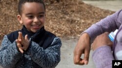 FILE - Nathan Aragaw, 4, mimics his mother, Mule Haile, of Washington, DC, as she instructs him on how to apply hand sanitizer between his fingers and on the backs of his hands after playing soccer at a public park, March 16, 2020.