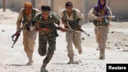 FILE - Kurdish fighters from the People's Protection Units (YPG) run across a street in Raqqa, Syria, July 3, 2017. 