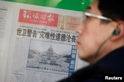 A man stands in front of a copy of the Global Times newspaper featuring an image of the U.S. Capitol during preparation for the inauguration of Joe Biden as the U.S. president, which is placed on a public display window in Beijing, Jan. 21, 2021.