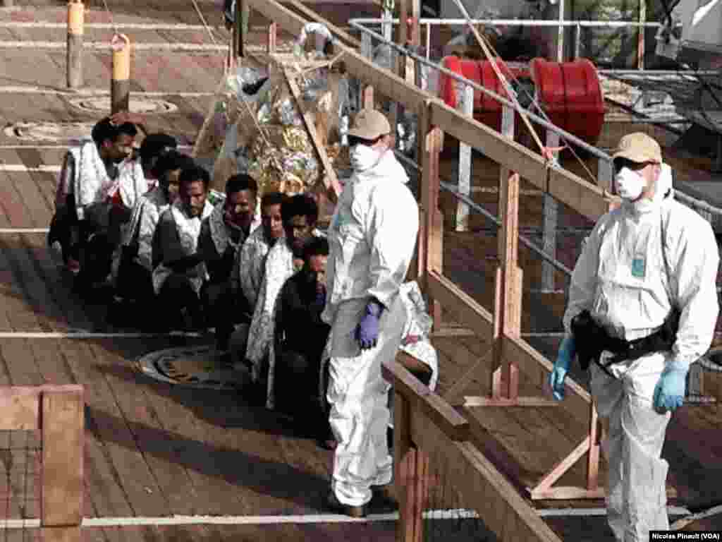 A Norwegian military is watching the migrants disembarking the boat in Messina, Sicily, Italy.