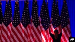 A worker adjusts the flags on stage ahead of an election night watch party for Republican presidential nominee former President Donald Trump in West Palm Beach, Fla., Nov. 5, 2024.