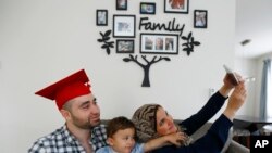 Mohamad Bassel Khair, left, holds his son, Sami Kahir, 2, as his wife Lama Alassil takes a photo of them to post on the Snapchat application during a photo session with The Associated Press in his home in Clifton, N.J. Khair, of Damascus, Syria, is graduating from New Jersey's Montclair State University with a master’s in nutrition and food science and is now seeking asylum in the U.S. for his family. 