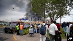 Para calon penumpang berjalan di trotoar saat pemadam kebakaran berupaya memadamkan api di bandara Internasional Jomo Kenyatta, Nairobi, Kenya (7/8).