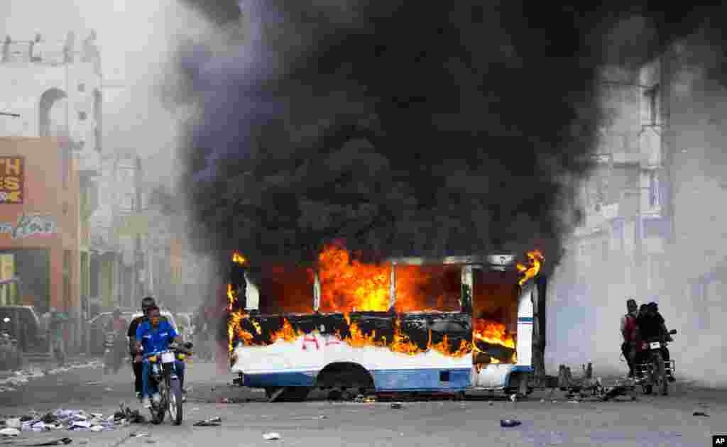 Motorcyclists pass a burning bus, set fire in Port-au-Prince, Haiti, during demonstrations protesting allegations of embezzlement from a Venezuelan program that provided the country with subsidized oil, Nov. 18, 2018.