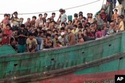 Migrants sit on their boat as they wait to be rescued by Acehnese fishermen on the sea off East Aceh, Indonesia, Wednesday, May 20, 2015. Hundreds of migrants stranded at sea for months were rescued and taken to Indonesia, officials said Wednesday, the la