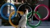 Seorang perempuan menggunakan masker pelindung berjalan melintas lambang Olimpiade, di depan Japan Olympics Museum di Tokyo, Jepang, di tengah wabah virus corona, 13 Maret 2020. (Foto: Reuters) 