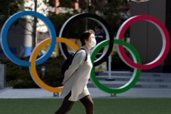 FILE - A woman wearing a protective face mask amid an outbreak of the coronavirus walks past Olympic rings displayed in front of the Japan Olympics Museum, in Tokyo, Japan, March 13, 2020.