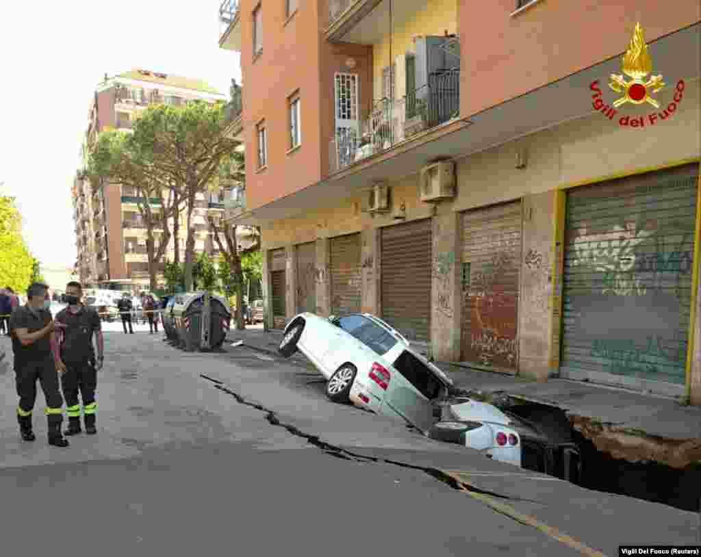 Cars are seen stuck sideways in a huge hole that has opened up next to an apartment building in Rome, Italy.