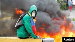 FILE - A demonstrator sits next to a fire barricade on a street during a rally against Venezuela's President Nicolas Maduro in Caracas, Venezuela, April 24, 2017.