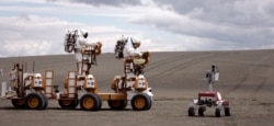 FILE - NASA astronauts in spacesuits drive their lunar truck near K-10 Red, June 10, 2008, in Moses Lake, Wash. NASA scientists and contractors spent two weeks in Moses Lake field testing some of the vehicles and robots that will be used on the moon.