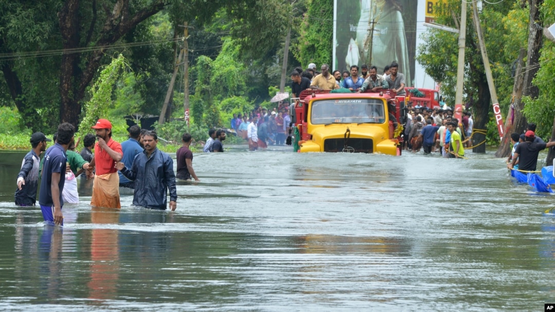 A truck carries people past a flooded road in Thrissur, in the southern Indian state of Kerala, Aug. 18, 2018. Rescuers used helicopters and boats Friday to evacuate thousands of people stranded on their rooftops following unprecedented flooding in the so