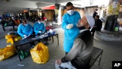 FILE - A health worker collects a swab sample from a man to test for COVID-19 in Jammu, India, Jan. 29, 2022.