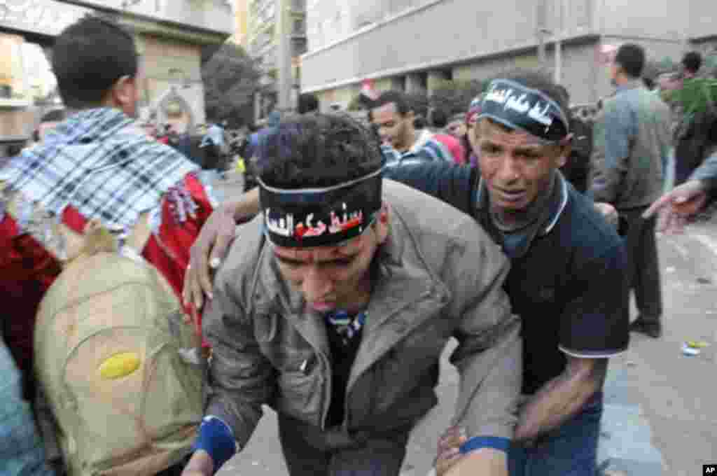An injured Egyptian protester is helped by another during clashes outside the US embassy in Cairo, Egypt, Friday, March 9, 2012. Several hundred protesters gathered Friday outside the U.S. Embassy in Cairo, raising their shoes at a picture of President Ba