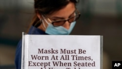Hostess Carla Alexander waits behind a sign that asks customers to wear masks at the Saint Arnold Brewing Company, June 26, 2020, in Houston. 