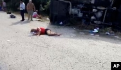 This video frame shows an injured woman lying on the road next to the overturned bus in which she was traveling, in Mahahual, Quintana Roo state, Mexico, Dec. 19, 2017.