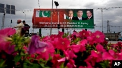 A Pakistani motorcyclist rides past a billboard showing pictures of Chinese President Xi Jinping, center, with Pakistan's President Mamnoon Hussain, left, and Prime Minister Nawaz Sharif welcoming Xi to Islamabad, Pakistan, April 19, 2015.