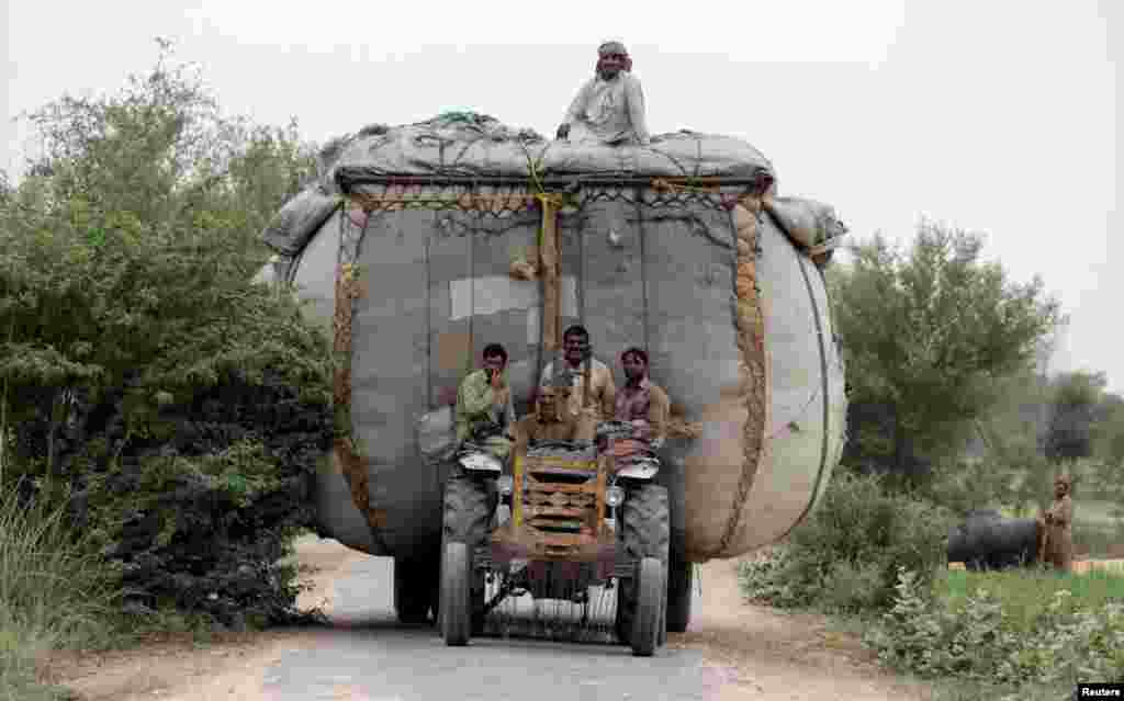 Para petani menumpang traktor yang kelebihan beban jerami di desa di luar Faisalabad, Pakistan.