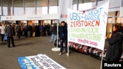 FILE - Protesters display a banner to protest against the financing of the Dakota Access oil pipeline by Swiss banks UBS and Credit Suisse as participants arrive ahead of the annual shareholder meeting of Swiss bank UBS in Basel, Switzerland, May 4, 2017. The banner reads "UBS + Credit Suisse destroy the Standing Rock Native American reserve." 