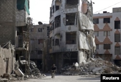 FILE - A man rides a bicycle past damaged buildings in the Douma neighborhood of Damascus, Nov. 26, 2015.