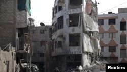 FILE - A man rides a bicycle past damaged buildings in the Douma neighborhood of Damascus, Nov. 26, 2015. 