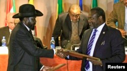 Presiden Sudan Selatan Salva Kiir (kiri) dan pemimpin pemberontak Riek Machar bertukar dokumen setelah menandatangani perjanjian gencatan senjata di Addis Ababa, Ethiopia, Februari 2015. 