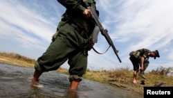 A soldier from the Kachin Independence Army puts on his shoes as he and his comrade cross a stream towards the front line in Laiza, Kachin state, January 29, 2013. 