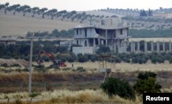 FILE - A masked man stands next to an excavator as it digs trenches in the Islamic State-held Syrian town of Jarablus, as they are pictured from the Turkish border town of Karkamis, in Gaziantep province, Turkey, Aug. 1, 2015.