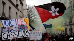 A sign depicting French politicians and reading "Here are the troublemakers" and flags with flares are displayed during the yellow vests 56th round demonstration in Paris, Dec. 7, 2019.