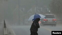 FILE - A man walks in a torrential downpour in Ellicott City, Maryland, April 30, 2014. 