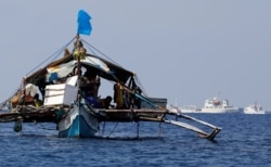 FILE - A Philippine fishing boat is seen anchored near China coast guard vessels patrolling at the disputed Scarborough Shoal, April 5, 2017.