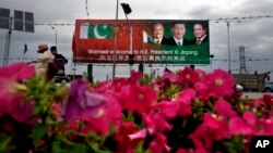 A Pakistani motorcyclist rides past a billboard showing pictures of Chinese President Xi Jinping, center, with Pakistan's President Mamnoon Hussain, left, and Prime Minister Nawaz Sharif welcoming Xi to Islamabad, Pakistan, April 19, 2015. 