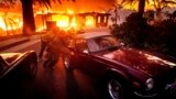 Firefighters and sheriff's deputies push a vintage car away from a burning home as the Mountain Fire burns in Camarillo, California, Nov. 6, 2024. 