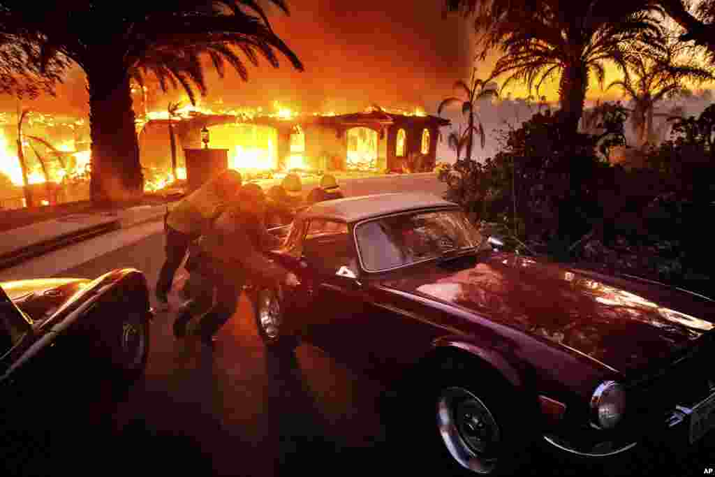 Firefighters and sheriff's deputies push a vintage car away from a burning home as the Mountain Fire burns in Camarillo, California, Nov. 6, 2024. 