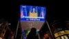 A woman sells balloons near a giant TV screen broadcasting news of U.S. President-elect Joe Biden delivers his speech, at a shopping mall in Beijing, Sunday, Nov. 8, 2020. 