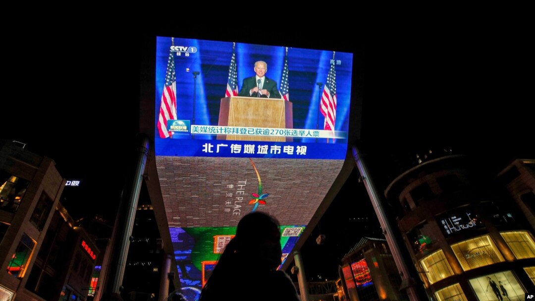 A woman sells balloons near a giant TV screen broadcasting a news of U.S. President-elect Joe Biden delivers his speech, at a shopping mall in Beijing, Nov. 8, 2020. 