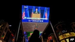 A woman sells balloons near a giant TV screen broadcasting news of U.S. President-elect Joe Biden delivers his speech, at a shopping mall in Beijing, Sunday, Nov. 8, 2020. 