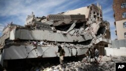 Men walk on the rubble of the Chamber of Trade and Industry headquarters after it was hit by a Saudi-led airstrike in Sana'a, Yemen, Tuesday, Jan. 5, 2016. 