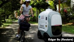 Seorang pengendara sepeda melewati Camello, robot pengantaran belanjaan, yang sedang mengantar belanjaan di Singapura, 6 April 2021. (Foto: Edgar Su/Reuters)