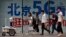 People walk toward a police robot mounted with surveillance cameras patrol past a 5G network advertisement at a shopping district in Beijing, May 15, 2019. 